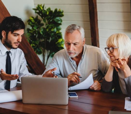 Smiling senior couple sit at lawyer broker designer office look at laptop listen to offer proposal of qualified specialist