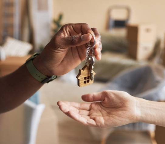 Hand of young African American male real estate agent passing key to new owner of apartment 