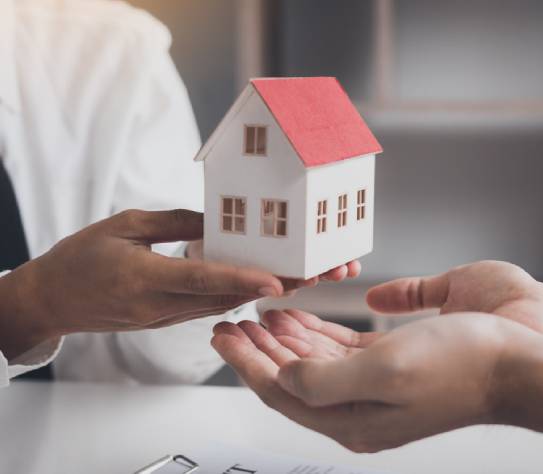 Real estate agent congratulations to new buyer by giving house model to client in the agency office.