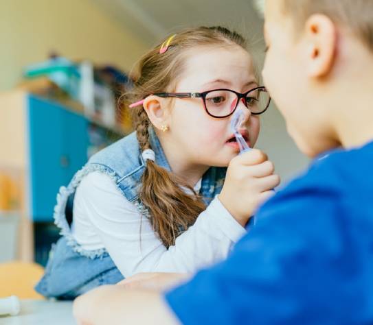 Integration of children with special needs concept. Little girl with down syndrome using dentist tool on boy as patient at school or kindergarten.